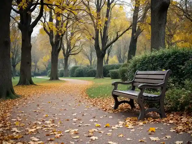 An empty park bench under autumn trees with fallen leaves on the path