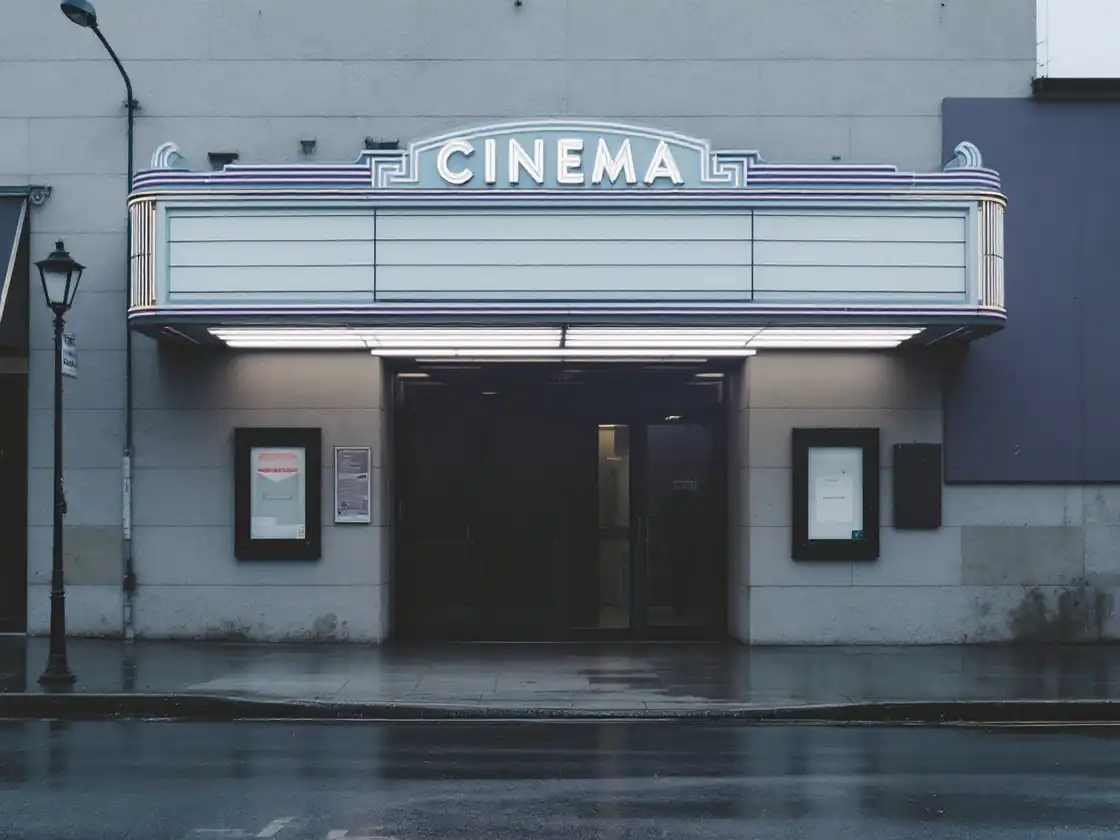 A small cinema entrance with a lit marquee and wet pavement