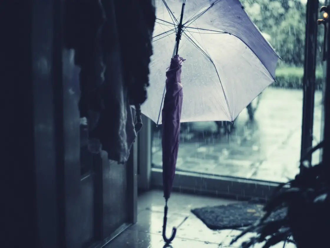 An open umbrella drying beside a rainy window