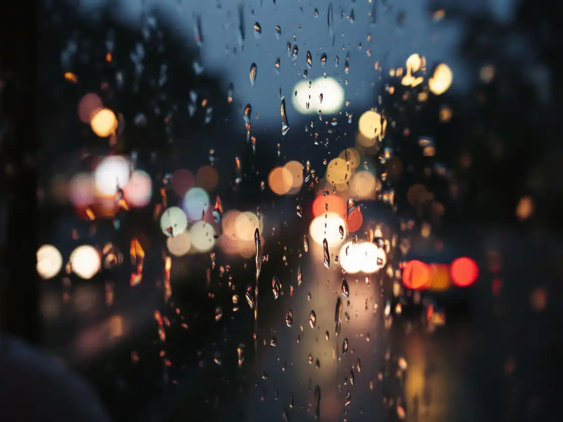 Rain drops on a bus window with blurred city lights at night
