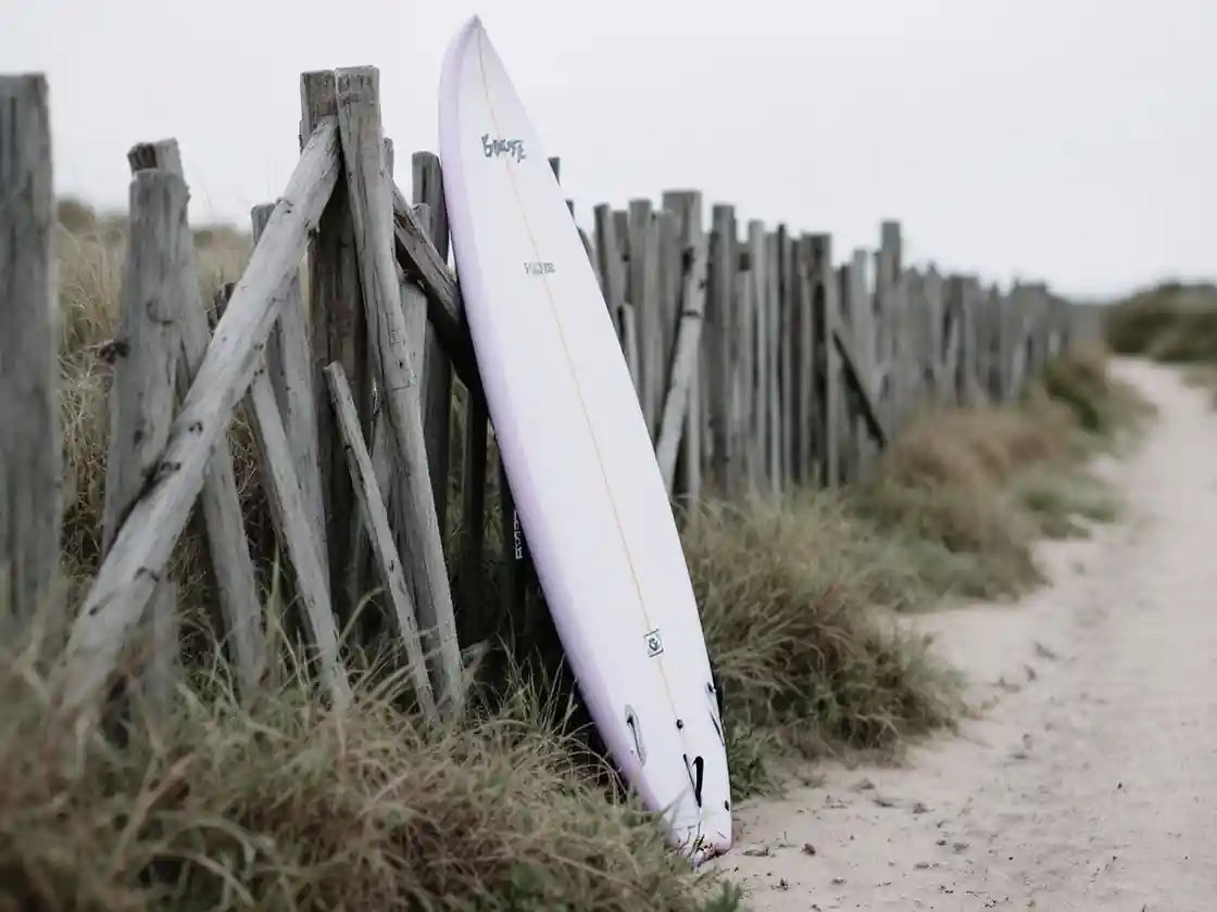 A surfboard leaning on a wooden fence by a beach path